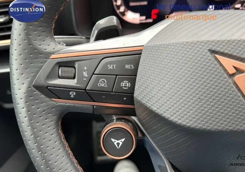 Gros plan sur le volant en cuir perforé noir du CUPRA Formentor blanc neige métal, avec commandes intégrées et logo distinctif.