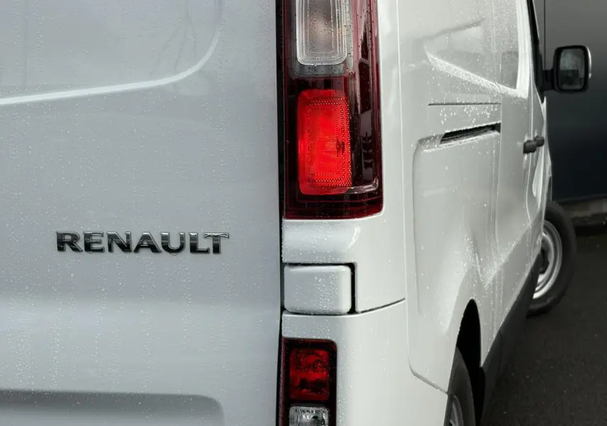 Détail arrière droit du Renault Trafic Fourgon blanc Glacier avec feux arrière et logo Renault sous la pluie.