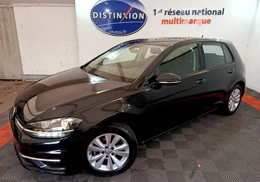 Volkswagen Golf noire vue en 3/4 avant droit, avec jantes argentées et phares allumés.