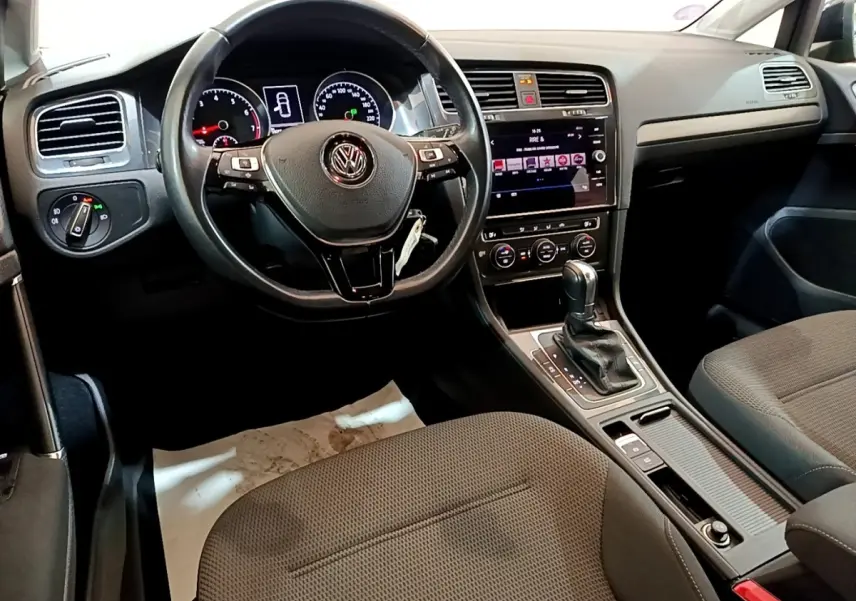 Vue intérieure centrée sur le volant cuir multifonctions et la console centrale d'une Volkswagen Golf noire de 2019.