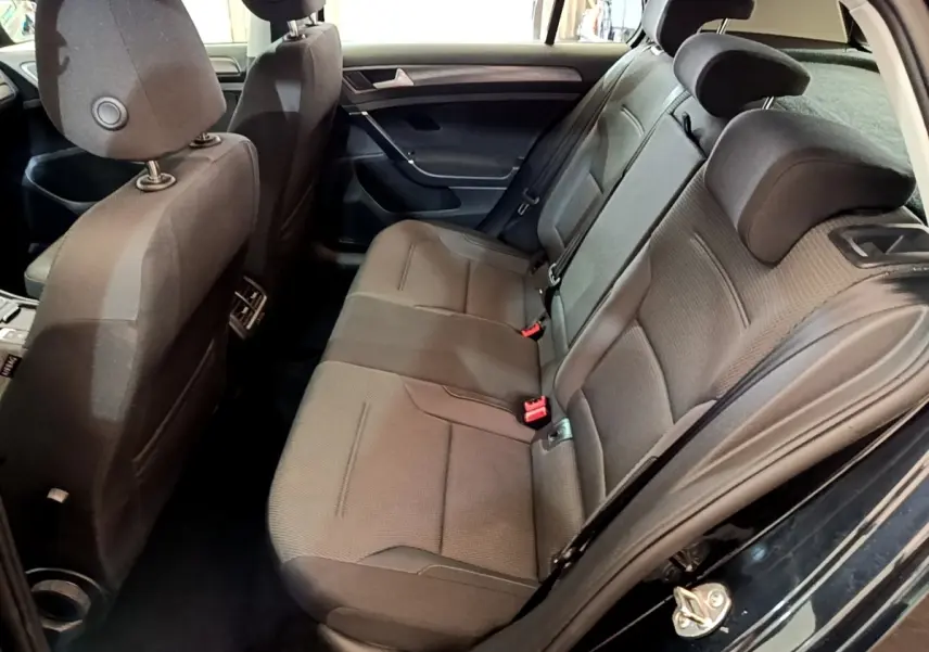 Vue intérieure côté droit sur la banquette arrière grise d’une Volkswagen Golf noire avec appuie-têtes et ceintures visibles.