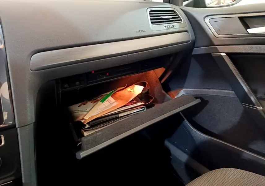 Vue intérieure côté passager d'une Volkswagen Golf noire de 2019, boîte auto, avec boîte à gants ouverte contenant des documents.