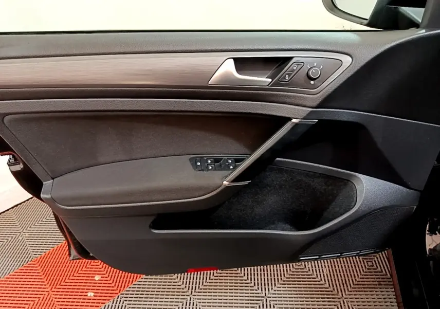 Vue intérieure du panneau de porte avant gauche de la Volkswagen Golf noire, avec commandes électriques et insert imitation bois.
