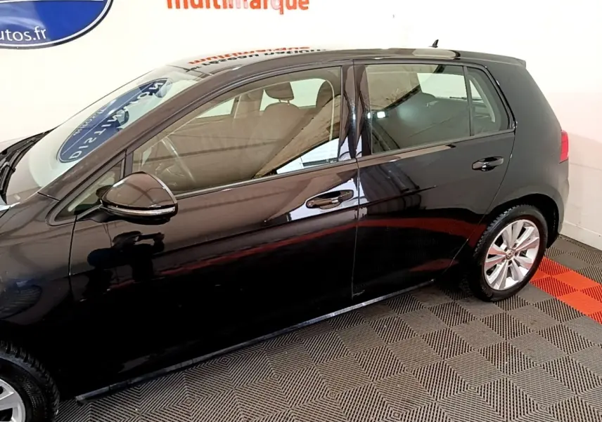 Vue de profil côté gauche d'une Volkswagen Golf noire 2019 stationnée sur sol damier noir et rouge.