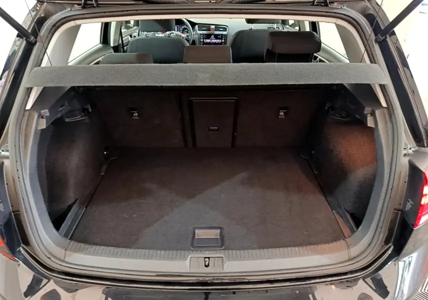 Coffre ouvert d’une Volkswagen Golf noire vue de l’arrière, montrant l’espace de chargement et la banquette arrière.