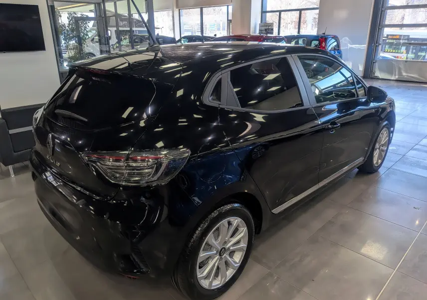 Vue 3/4 arrière droite d'une Renault Clio V noire 2025 en showroom, avec jantes alliage et vitres teintées.