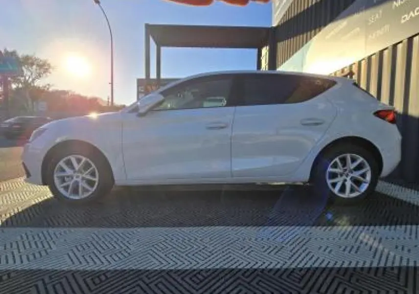 Profil côté gauche d'une SEAT LEON blanche 2024 stationnée, avec jantes alliage et arrière légèrement en ombre.