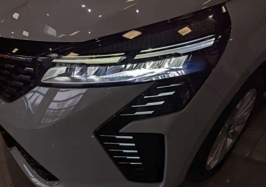 Gros plan sur le phare avant droit de la Renault Clio V 2025 en gris Rafale, avec détails lumineux modernes et calandre noire.