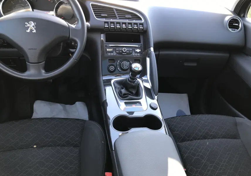Intérieur noir de la Peugeot 3008 Business, vue de face sur le volant, levier de vitesse manuel et console centrale brillante.