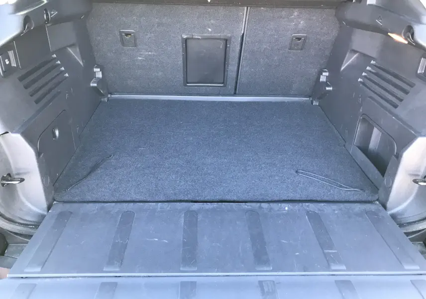 Coffre ouvert vu de l'arrière d'un Peugeot 3008 Business bleu Bourrasque avec tapis de sol gris et rangements latéraux.