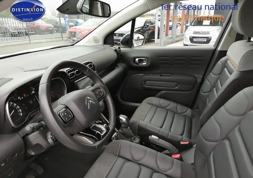 Intérieur du Citroën C3 Aircross blanc polar, vue côté conducteur montrant le tableau de bord et les sièges noirs en cuir.
