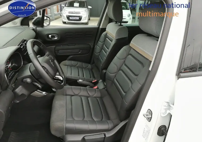 Vue intérieure côté conducteur d'une Citroën C3 Aircross blanc polar, sièges en cuir noir et tissu gris clair.