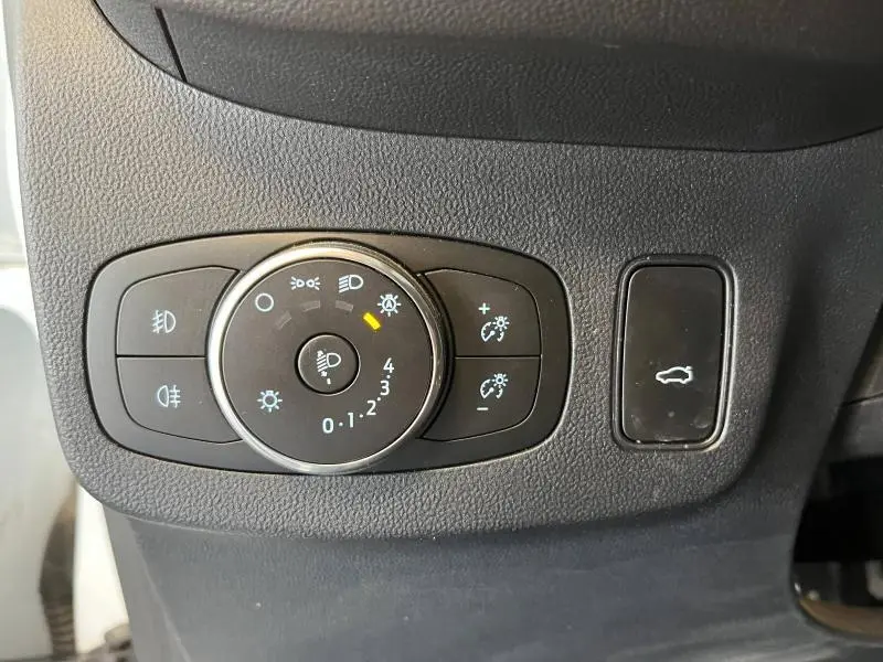 Vue rapprochée du panneau de commande des phares et du bouton d'ouverture du hayon électrique dans un Ford Puma blanc glacier 2022.