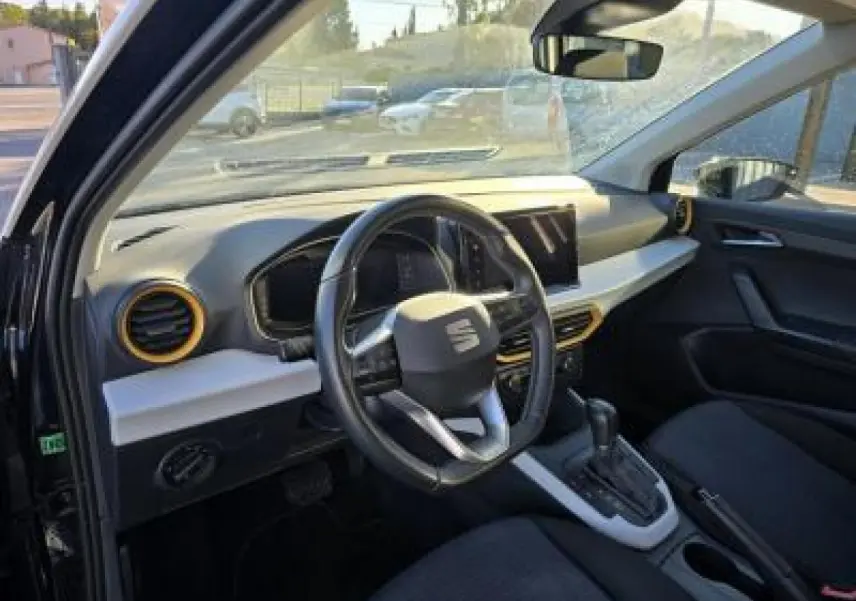 Intérieur du SEAT Arona 2024 vu côté conducteur, volant cuir multifonction et tableau de bord clair avec touches jaunes.