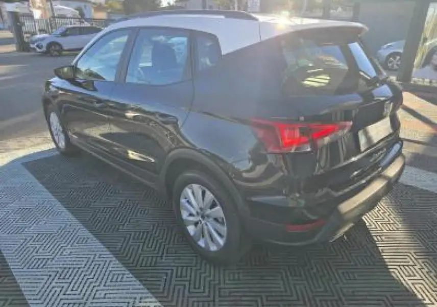 Vue 3/4 arrière droite d'un SEAT Arona noir minuit avec toit contrasté, jantes alliage et feux arrière LED allumés.