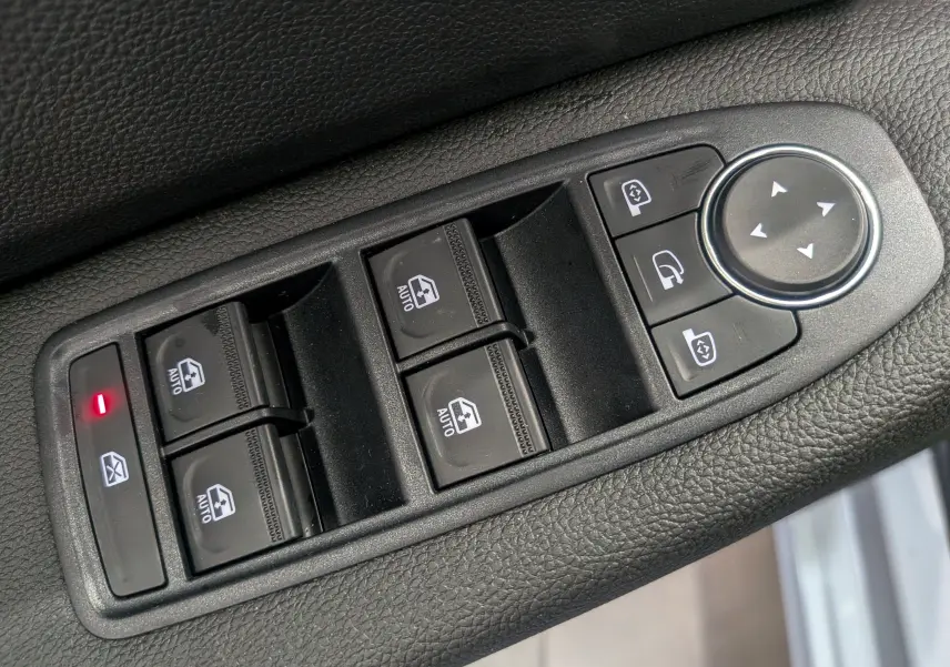 Gros plan sur les commandes de lève-vitres et rétroviseurs électriques sur la porte côté gauche d’une Renault Clio V gris Rafale.