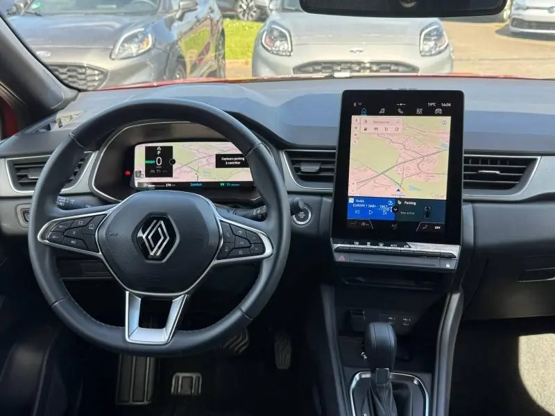 Vue intérieure frontale du tableau de bord du Renault Captur rouge 2025 avec écran tactile vertical et volant multifonction.