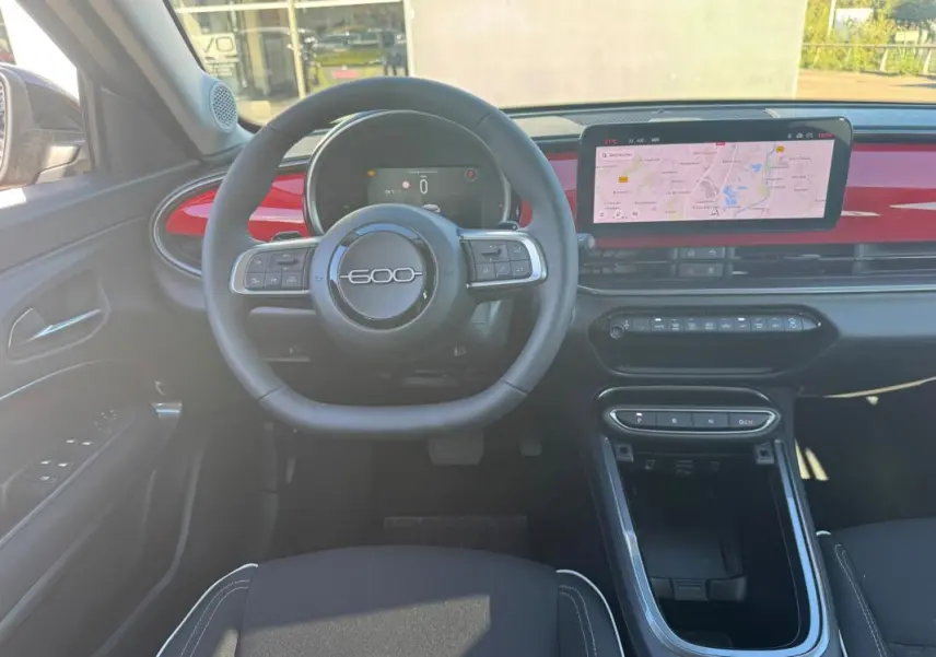 Vue intérieure frontale du tableau de bord de la FIAT 600 rouge 2025, avec volant marqué "600" et écran tactile GPS.
