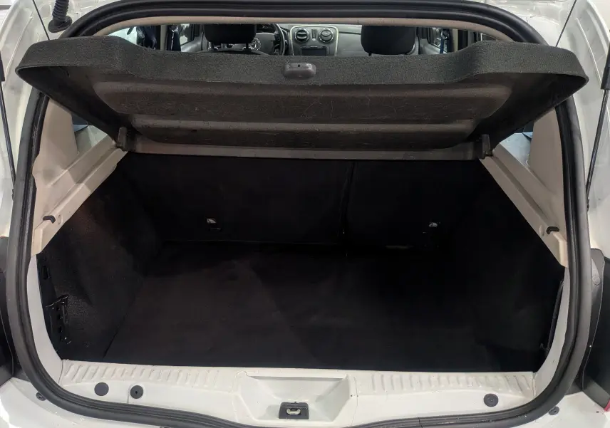 Coffre ouvert vu de l'arrière d'une Dacia Sandero blanc glacier, montrant l'espace de chargement vide et l'intérieur noir.