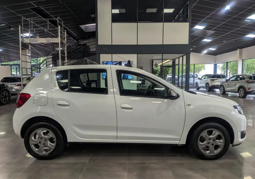 Profil côté gauche d'une Dacia Sandero blanc glacier de 2015, compacte et sobre, en intérieur de showroom.