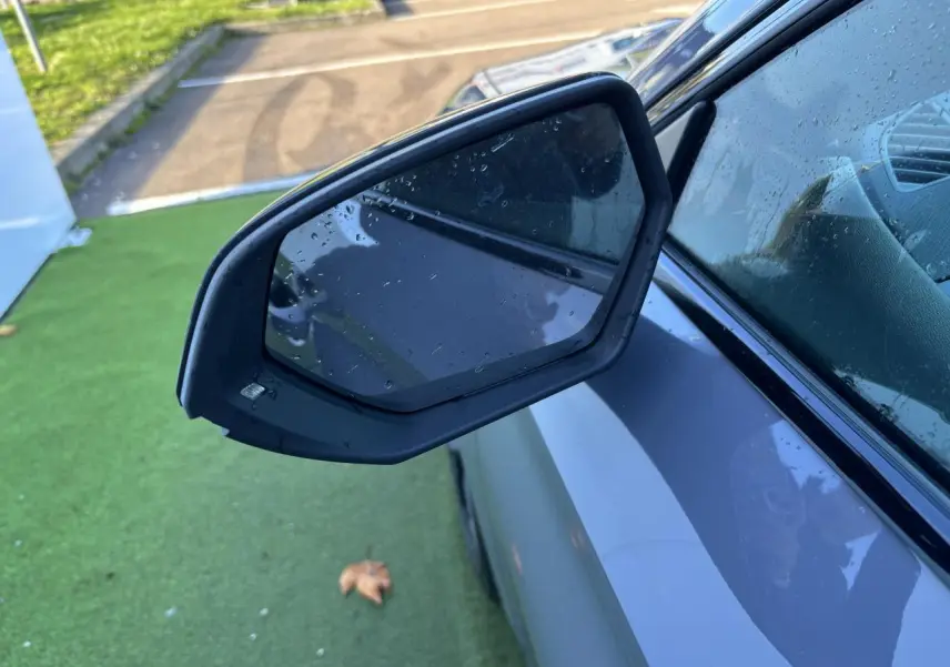 Gros plan sur le rétroviseur côté gauche d'une CUPRA Leon 2024 gris Graphene avec gouttes d'eau visibles.