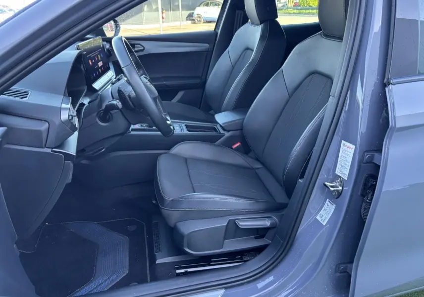 Vue côté conducteur de l'intérieur gris graphene du CUPRA Leon 2024, avec sièges en cuir et écran tactile central.