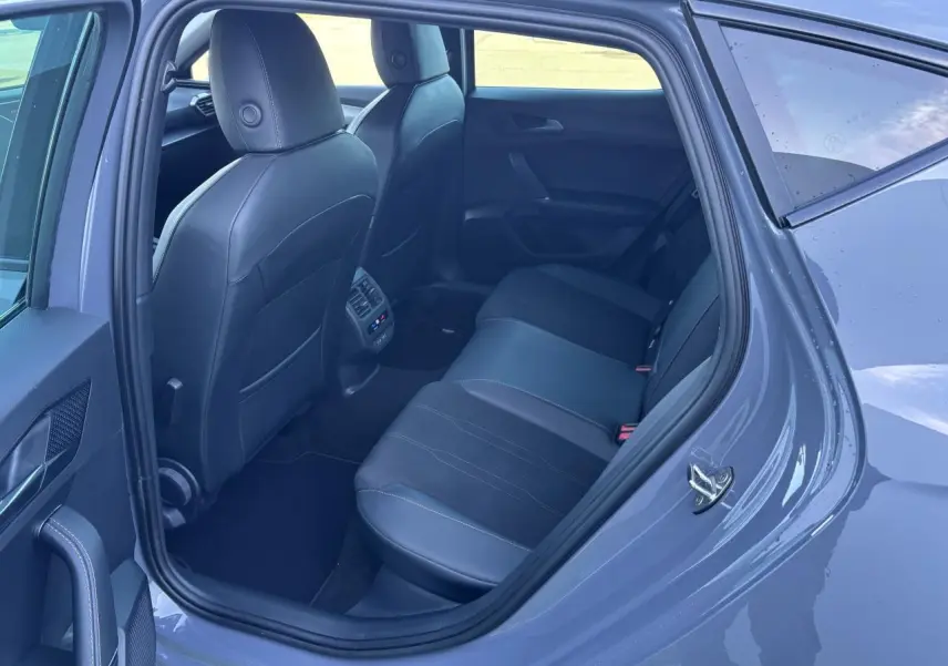 Vue côté arrière gauche de l'habitacle d'une CUPRA Leon gris Graphene, montrant les sièges arrière en cuir noir et les commandes de climatisation.