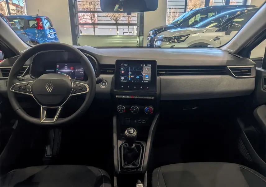 Vue intérieure avant de la Renault Clio V 2025, tableau de bord moderne avec écran tactile et levier de vitesse manuel.