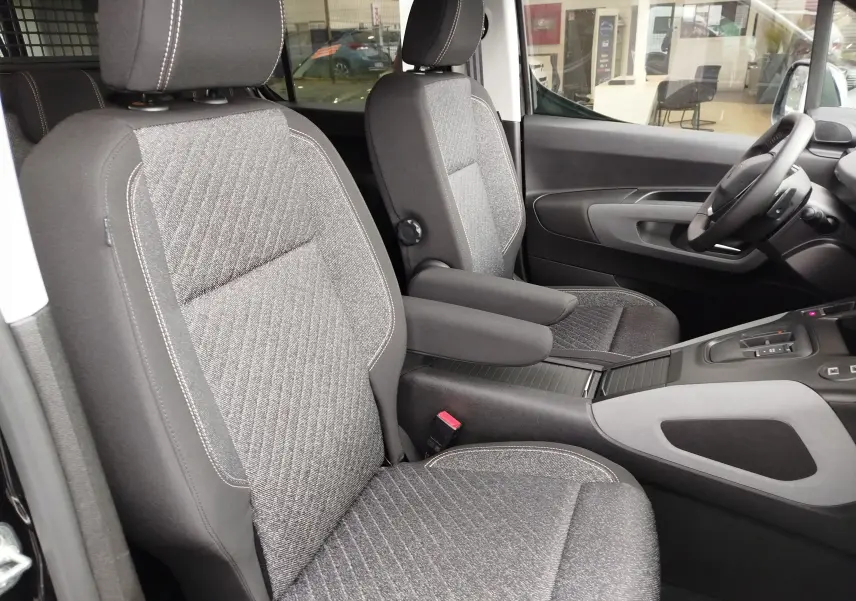 Vue intérieure côté conducteur du Peugeot Rifter 2026, sièges tissu gris avec accoudoir central et volant visible.