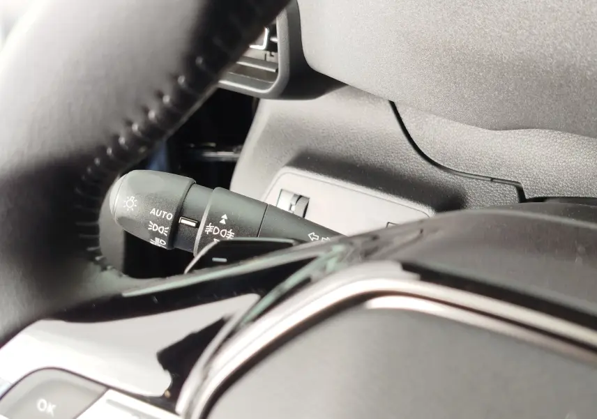 Gros plan sur la manette des feux et clignotants à gauche du volant dans l’habitacle gris du Peugeot Rifter noir Perla Nera.