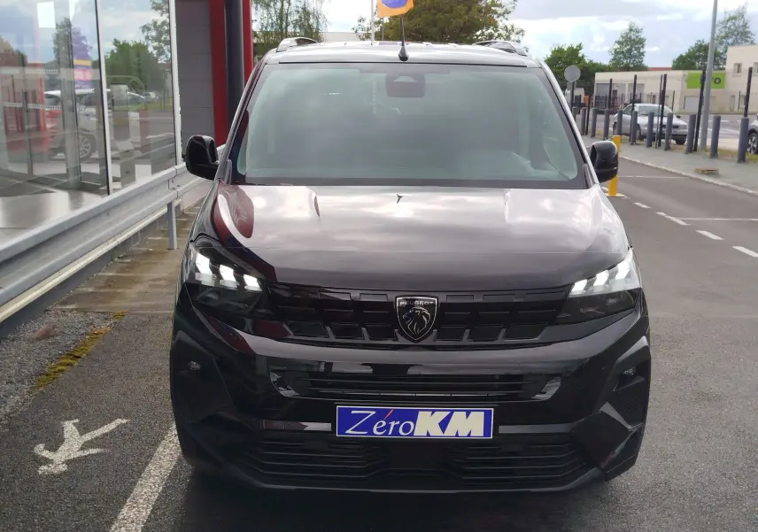 Vue avant d'un Peugeot Rifter noir Perla Nera 2026 avec phares LED allumés et logo lion bien visible.