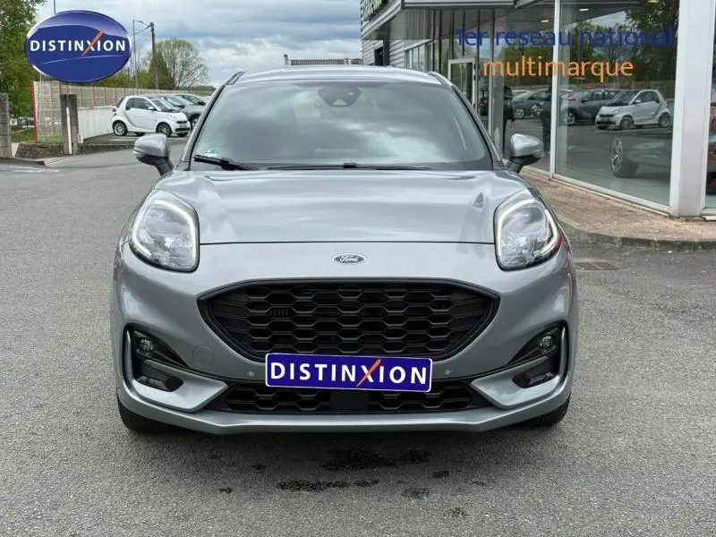 Vue avant d'un Ford Puma 2024 gris métallisé avec calandre noire et logo Ford visible sur un parking.
