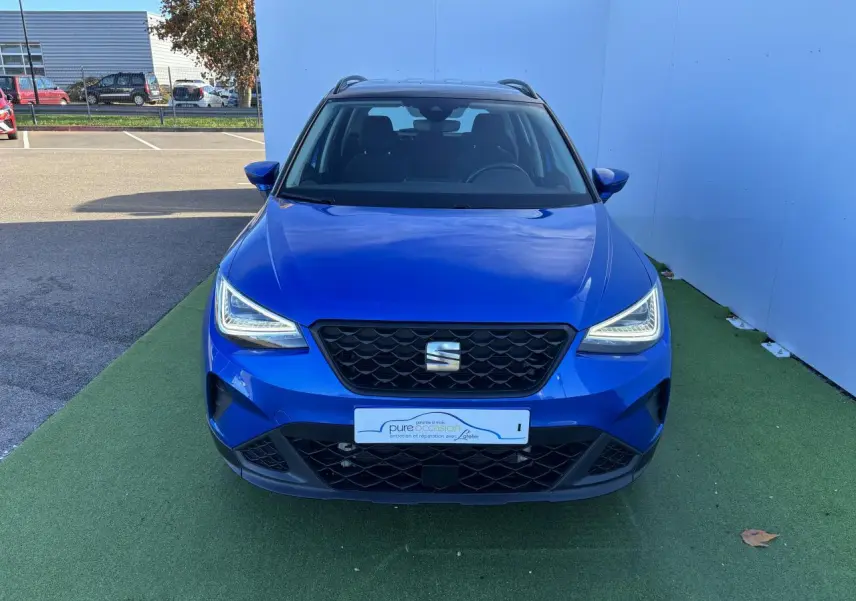 Vue frontale d'un SEAT Arona bleu saphir avec toit noir, phares LED allumés et calandre noire distinctive.