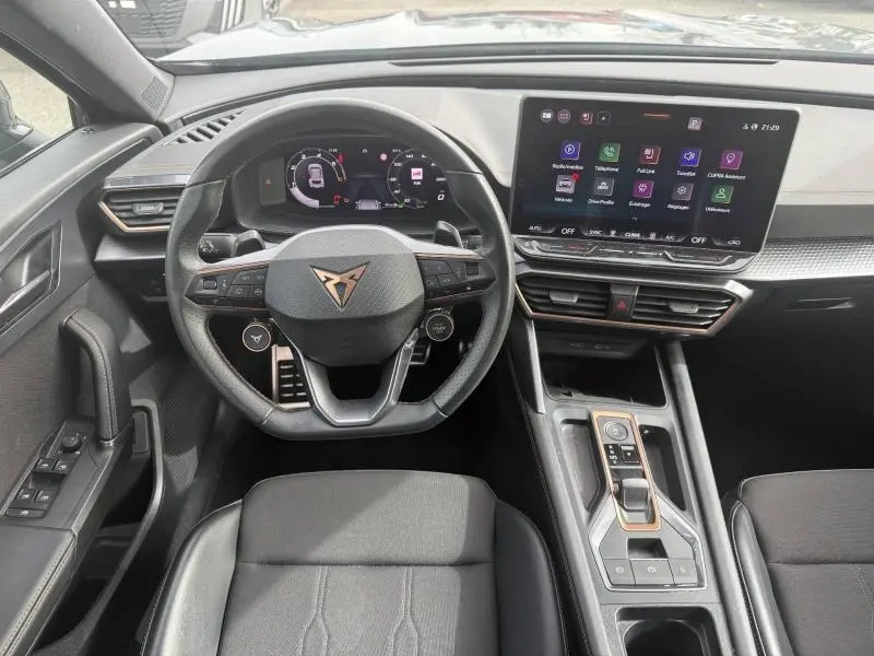 Vue intérieure avant du tableau de bord et volant cuir noir du CUPRA Formentor bleu, avec écran tactile central allumé.