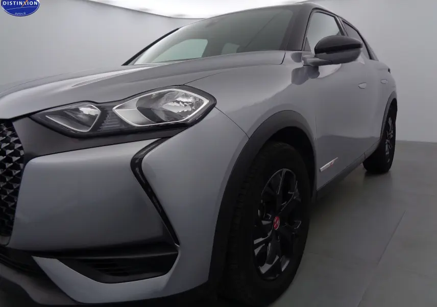 Vue 3/4 avant droit du DS3 Crossback gris Artense métal avec jantes noires et calandre distinctive en losange.