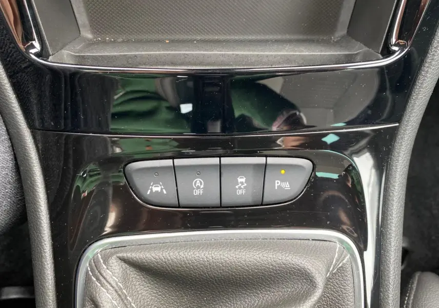 Gros plan sur la console centrale noire brillante de l'Opel Astra 2021, avec boutons d'aide au stationnement et levier de vitesse.