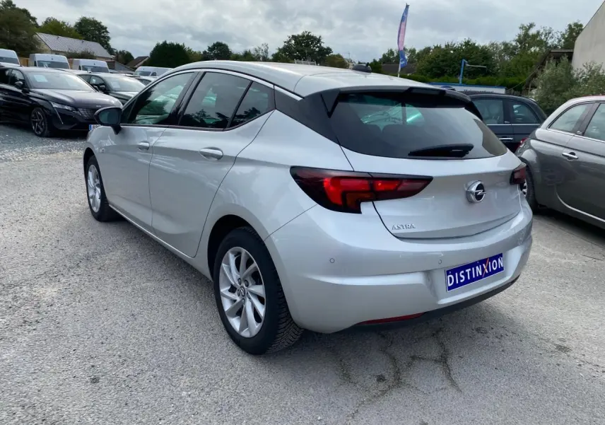 Opel Astra 2021 couleur argent vue 3/4 arrière droit avec vitres surteintées et jantes alliage 16 pouces.