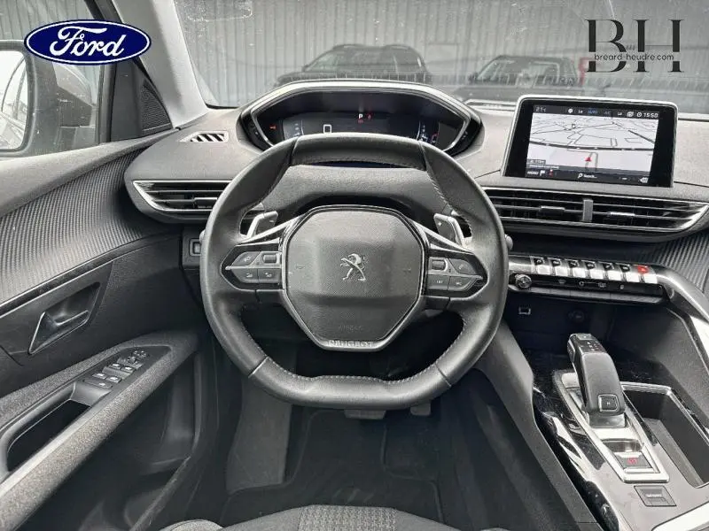 Vue intérieure centrée sur le volant cuir multifonction du Peugeot 5008 gris Artense avec écran tactile et levier de boîte auto.