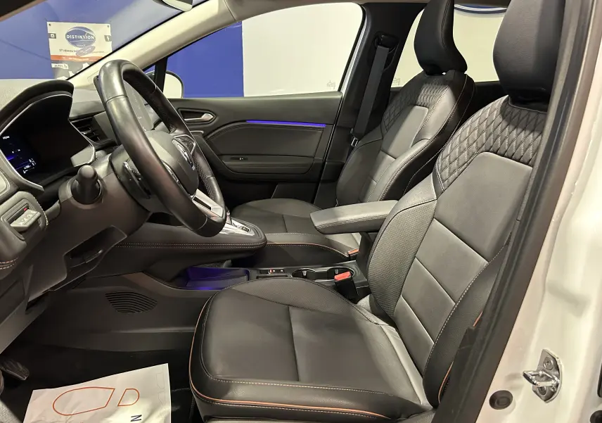 Vue intérieure côté conducteur du Renault Captur blanc nacré 2022, sièges cuir noirs avec surpiqûres contrastées et tableau de bord moderne.