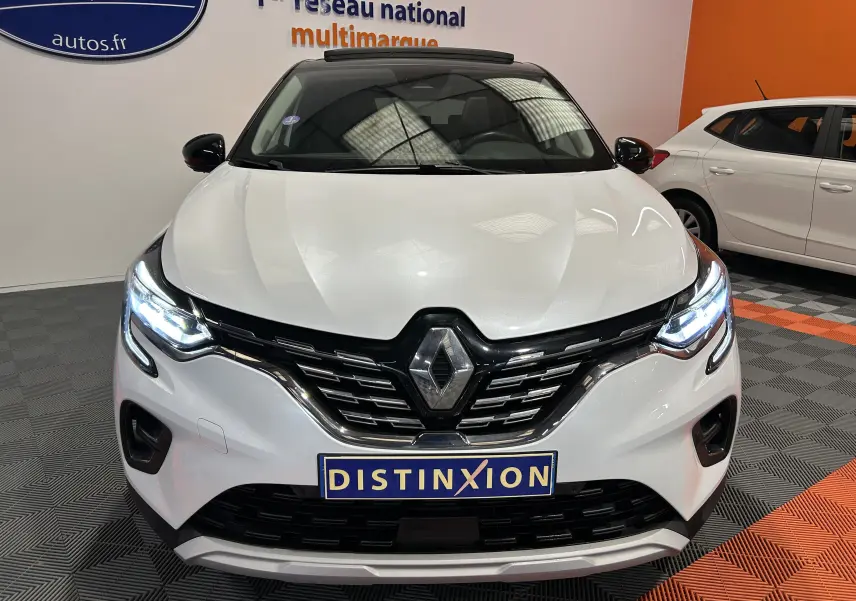 Vue frontale d'un Renault Captur blanc nacré 2022 avec phares allumés et toit ouvrant visible en intérieur showroom.