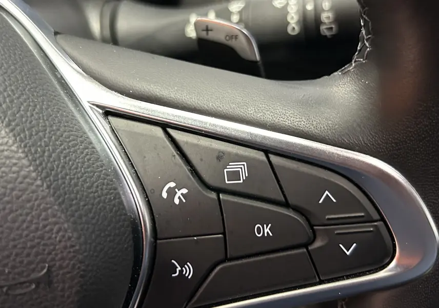 Gros plan sur les commandes multifonctions du volant en cuir noir du Renault Captur II Iconic blanc nacré.