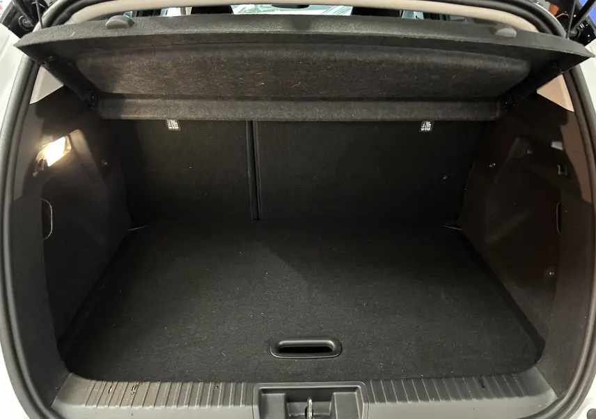Coffre ouvert vu de l'arrière d'un Renault Captur blanc nacré, intérieur noir et éclairage latéral allumé.