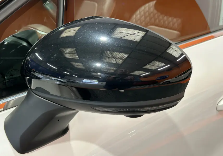 Rétroviseur extérieur noir brillant côté gauche du Renault Captur blanc nacré avec siège cuir beige visible à l'intérieur.