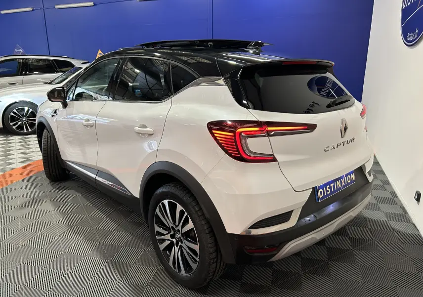 Vue 3/4 arrière droite du Renault Captur blanc nacré avec toit noir ouvrant et feux LED distinctifs dans un showroom.