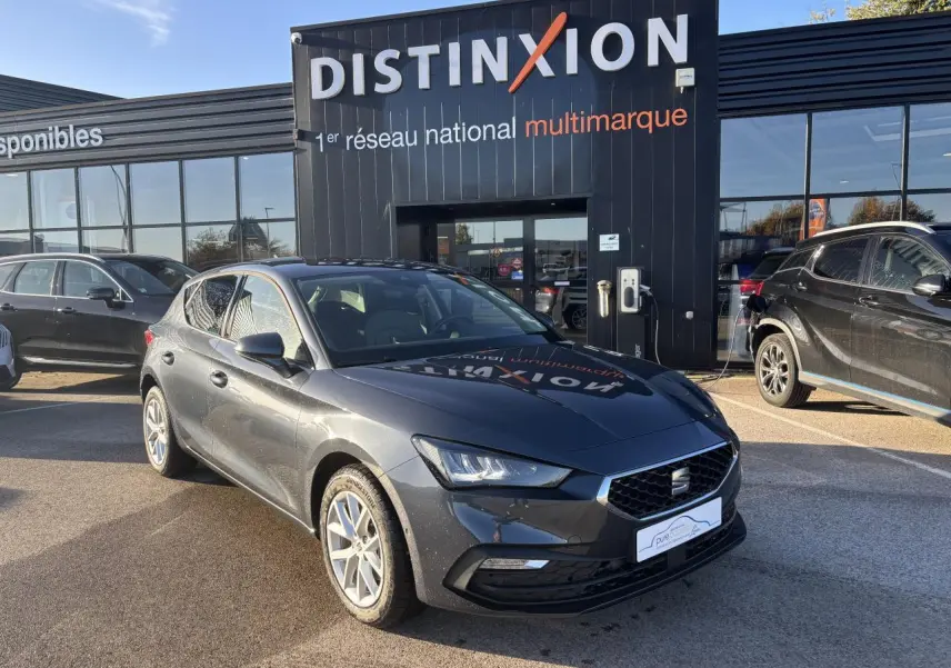 SEAT Leon IV gris magnetic vue 3/4 avant droit, jantes alliage 16 pouces, stationnée devant un showroom Distinxion.