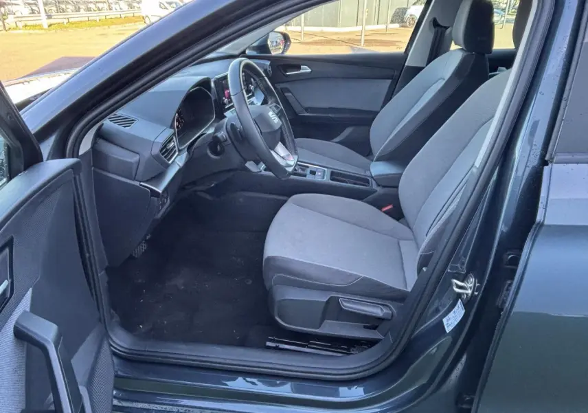 Intérieur côté conducteur d'une SEAT Leon gris magnetic 2024, montrant sièges tissu et tableau de bord moderne.