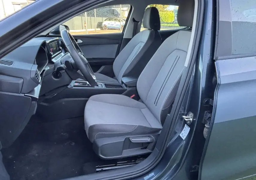 Vue intérieure côté conducteur de la SEAT LEON IV gris magnetic, montrant les sièges tissu et le volant multifonction cuir.