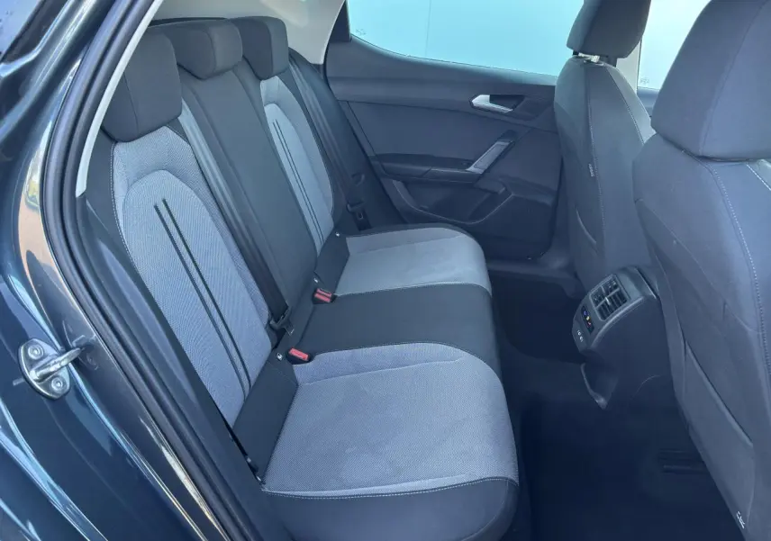 Vue intérieure côté arrière gauche du SEAT Leon gris magnetic, montrant la banquette arrière bicolore et les aérateurs centraux.