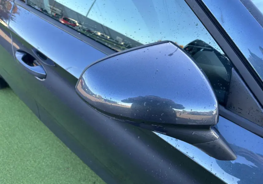 Rétroviseur côté gauche gris magnetic d'une SEAT Leon 2024 avec portière et poignée visibles sous la pluie.