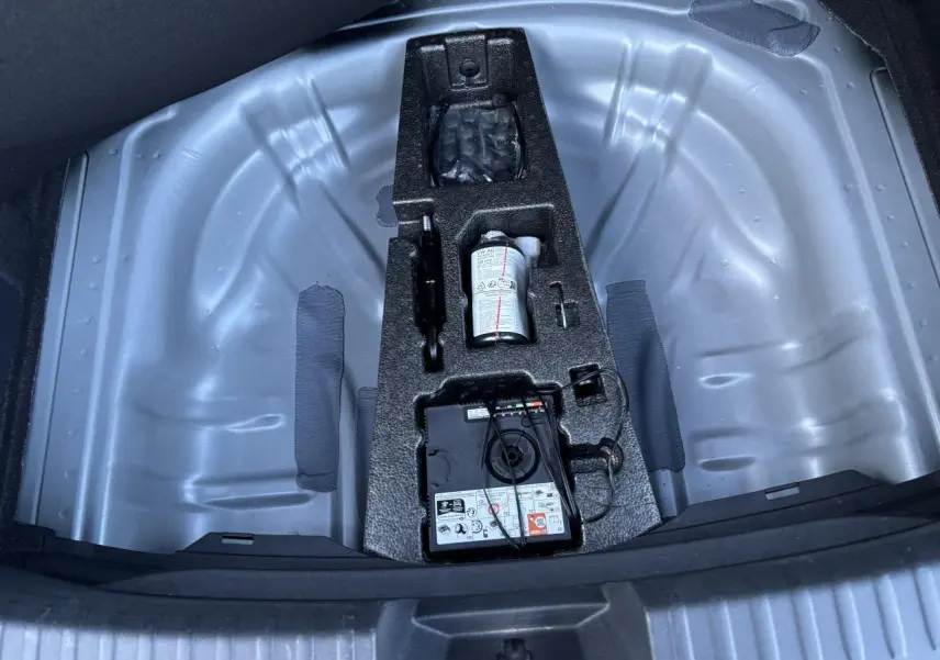 Vue plongeante sur le coffre ouvert d'une SEAT LEON gris magnetic, montrant le rangement pour roue de secours et kit de réparation.